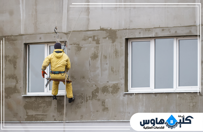 ترميم حمامات بجدة 0558994637 شركة كلين هاوس عامل معلق بالحبال يعالج واجهة مبنى خارجية لتنفيذ أعمال الصيانة وتجديد الأسطح وتحسين مظهر العقار.